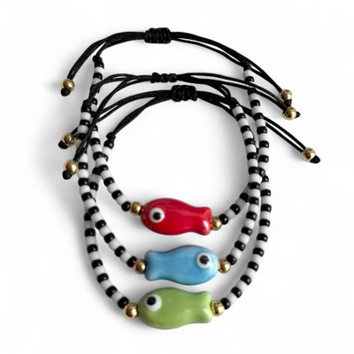 Set of three colorful fish-shaped beads on a black cord with gold accents against a white background.